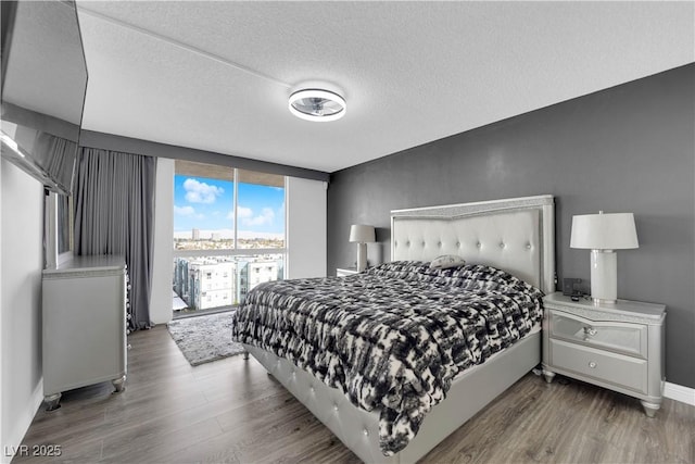 bedroom featuring baseboards, a textured ceiling, wood finished floors, and a wall of windows