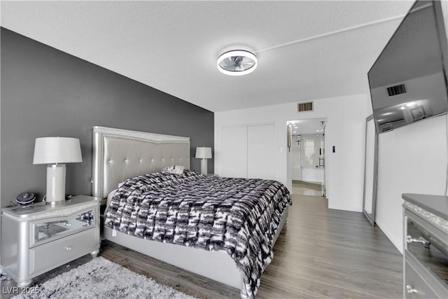bedroom with a closet, a textured ceiling, visible vents, and wood finished floors