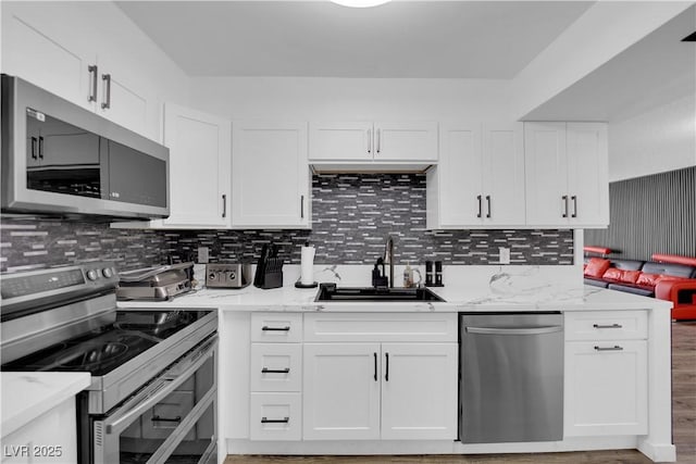 kitchen with white cabinetry, tasteful backsplash, a sink, light stone counters, and appliances with stainless steel finishes