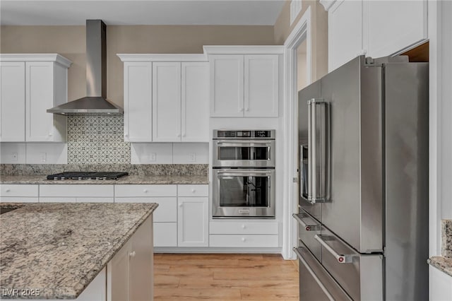 10348 Bressana Dr, Las Vegas, NV 89135 - kitchen featuring stainless steel appliances, wall chimney exhaust hood, white cabinets, and light wood-type flooring