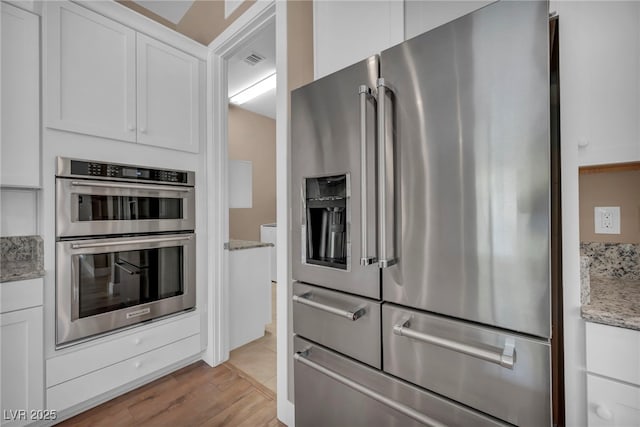 10348 Bressana Dr, Las Vegas, NV 89135 - kitchen featuring appliances with stainless steel finishes, white cabinets, light stone countertops, and light wood-style flooring