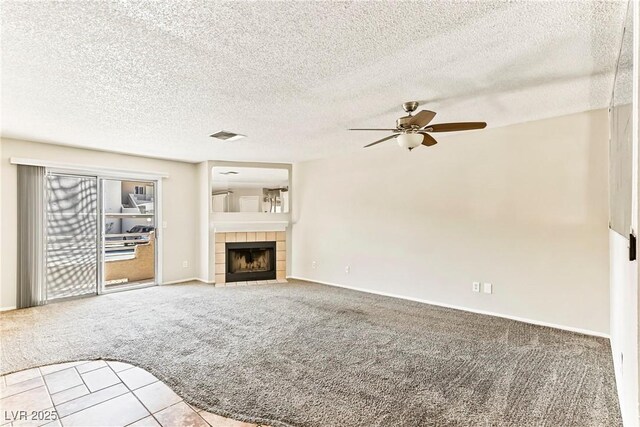 unfurnished living room with ceiling fan, a tiled fireplace, baseboards, carpet flooring, and visible vents