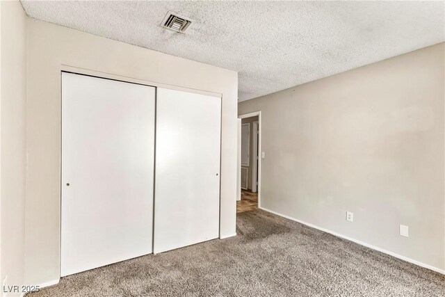 unfurnished bedroom featuring carpet flooring, a textured ceiling, visible vents, baseboards, and a closet
