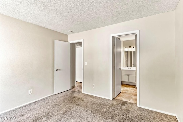 unfurnished bedroom featuring carpet, connected bathroom, a sink, baseboards, and a textured ceiling
