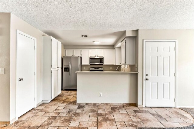 kitchen with a peninsula, visible vents, a textured ceiling, and appliances with stainless steel finishes