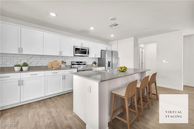 6952 Crimson Shadow St, North Las Vegas, NV 89086 - kitchen with appliances with stainless steel finishes, a center island with sink, white cabinetry, light stone countertops, and recessed lighting