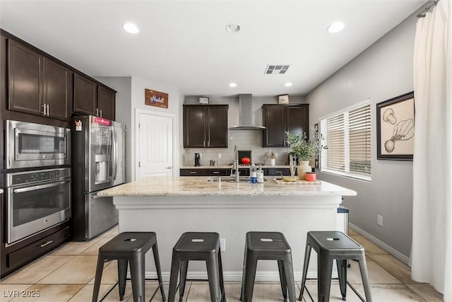 kitchen with a sink, wall chimney exhaust hood, a kitchen breakfast bar, appliances with stainless steel finishes, and visible vents