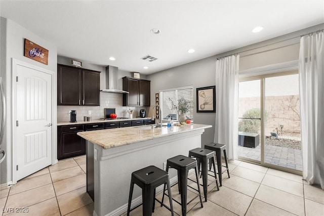 kitchen with stainless steel gas stovetop, decorative backsplash, visible vents, a breakfast bar, and wall chimney range hood