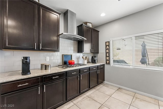 kitchen featuring stainless steel gas cooktop, dark brown cabinets, tasteful backsplash, wall chimney range hood, and light tile patterned floors