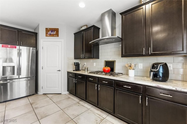 kitchen with light stone counters, wall chimney exhaust hood, appliances with stainless steel finishes, light tile patterned floors, and decorative backsplash