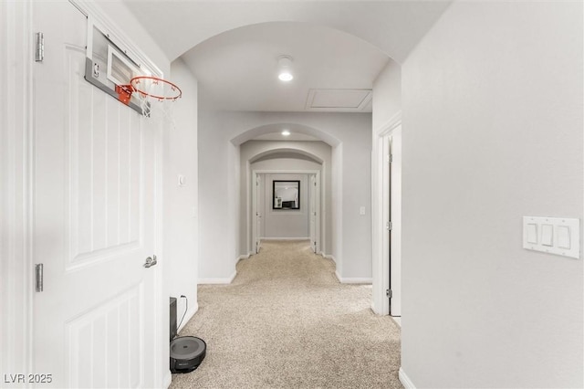 hallway featuring arched walkways, baseboards, and light colored carpet