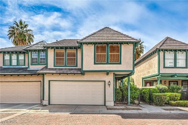 view of property featuring a tiled roof, stucco siding, an attached garage, and driveway