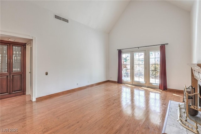 unfurnished living room with high vaulted ceiling, a fireplace with raised hearth, baseboards, visible vents, and light wood-style floors