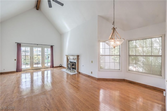 unfurnished living room with high vaulted ceiling, beam ceiling, a ceiling fan, wood finished floors, and baseboards