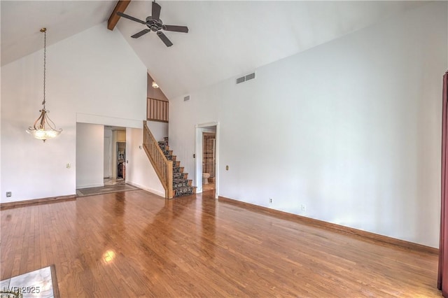 unfurnished living room with visible vents, beamed ceiling, wood finished floors, stairway, and a ceiling fan