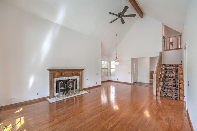 unfurnished living room with beam ceiling, stairway, a ceiling fan, a fireplace, and wood finished floors
