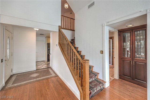 stairs with a high ceiling, visible vents, baseboards, and wood finished floors