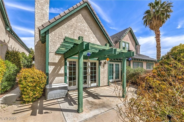 rear view of property featuring a tiled roof, a patio, stucco siding, french doors, and a pergola