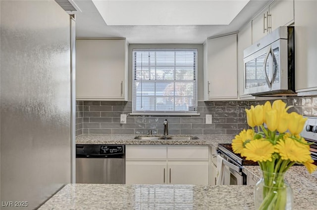 kitchen featuring light stone counters, white cabinetry, backsplash, stainless steel appliances, and a sink