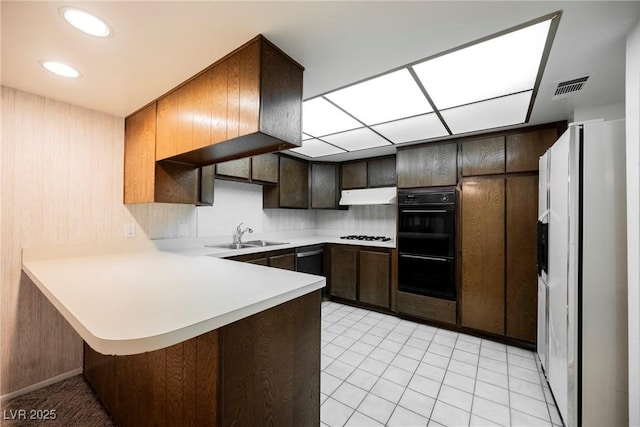 kitchen with under cabinet range hood, light countertops, a sink, visible vents, and a peninsula