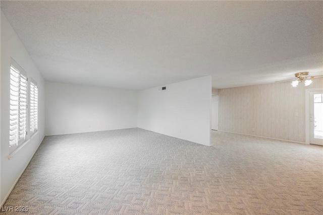 empty room with a textured ceiling, ceiling fan, a wealth of natural light, and light colored carpet