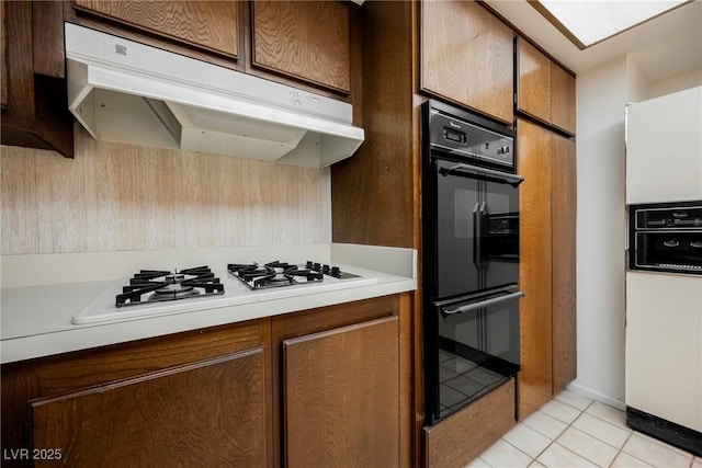 kitchen with light tile patterned floors, light countertops, under cabinet range hood, and white appliances
