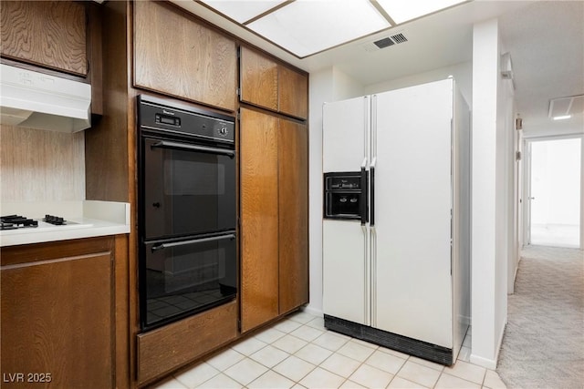 kitchen featuring light countertops, light tile patterned flooring, ventilation hood, white appliances, and brown cabinetry