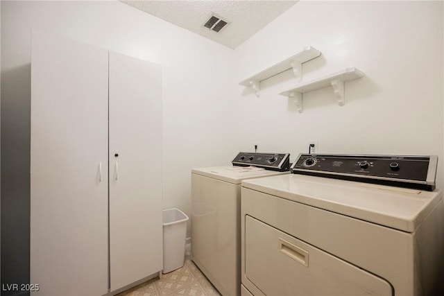 laundry area featuring a textured ceiling, washing machine and clothes dryer, visible vents, light floors, and laundry area