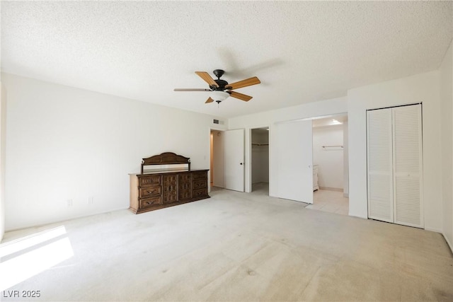 unfurnished bedroom featuring connected bathroom, visible vents, light carpet, two closets, and a ceiling fan