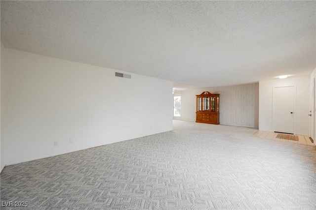 unfurnished living room featuring a textured ceiling, visible vents, and light carpet