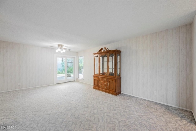 empty room featuring a textured ceiling, wallpapered walls, baseboards, carpet floors, and a ceiling fan