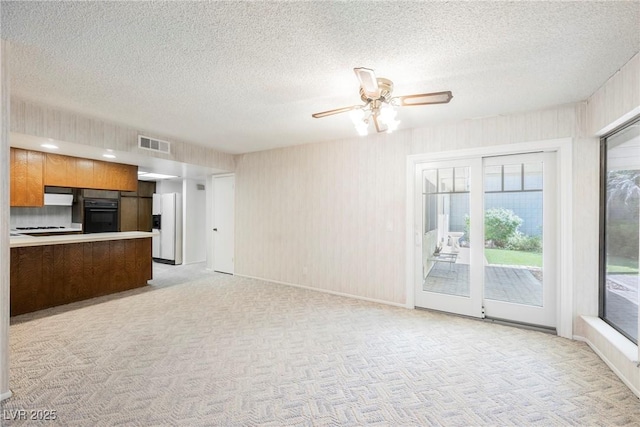 unfurnished living room featuring a textured ceiling, visible vents, and light carpet