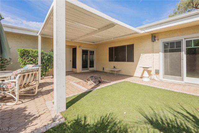 back of property with stucco siding, a patio area, and a lawn