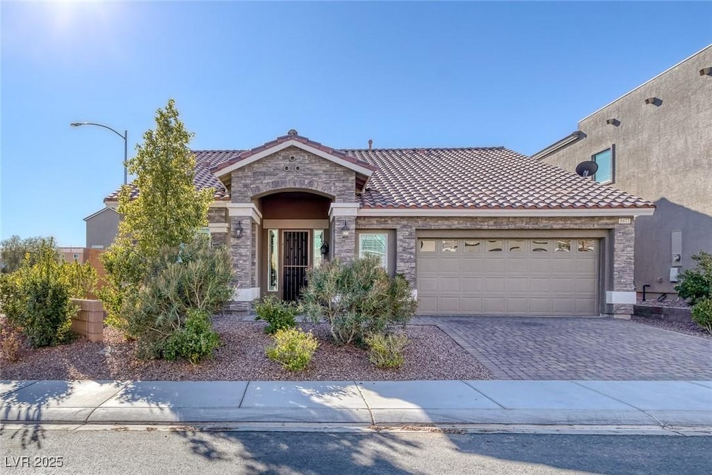 view of front of home with stone siding, a tiled roof, decorative driveway, an attached garage, and stucco siding