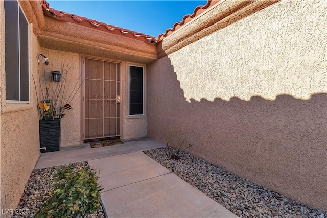 view of exterior entry with stucco siding and a tile roof