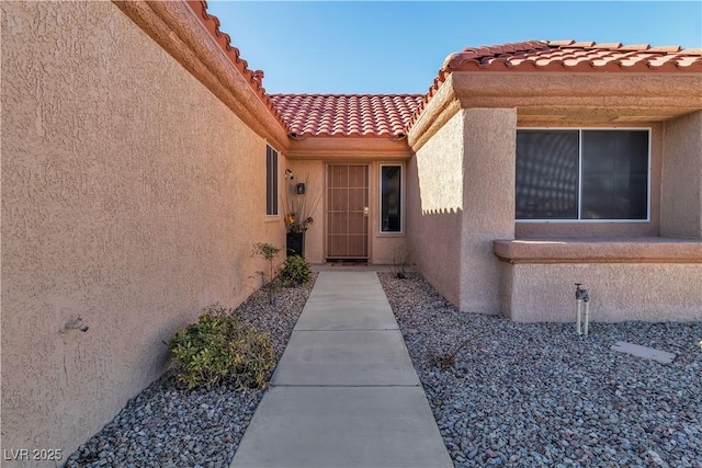 view of exterior entry featuring a tiled roof and stucco siding