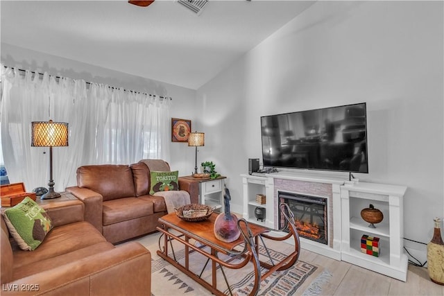 living area featuring a glass covered fireplace, visible vents, wood finished floors, and vaulted ceiling