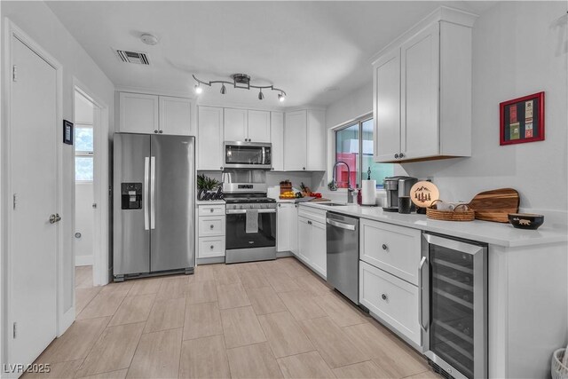 kitchen with a sink, stainless steel appliances, visible vents, white cabinetry, and beverage cooler