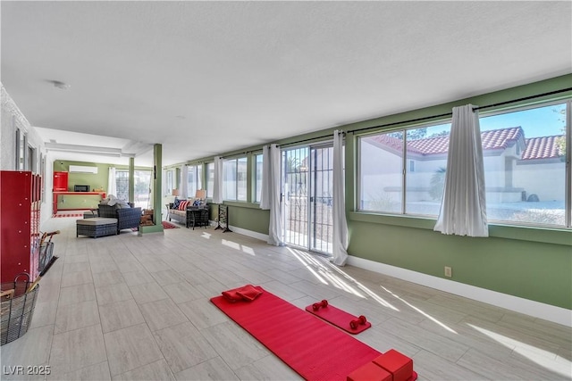 sunroom featuring baseboards, a healthy amount of sunlight, and a wall mounted AC