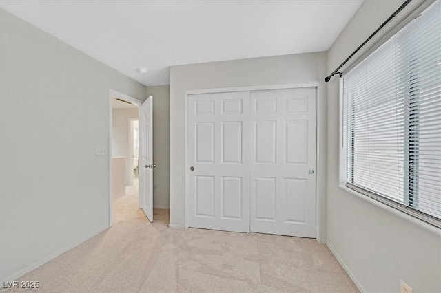 unfurnished bedroom featuring light colored carpet, baseboards, multiple windows, and a closet