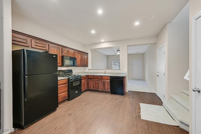 kitchen featuring a sink, ceiling fan, light countertops, black appliances, and light wood finished floors