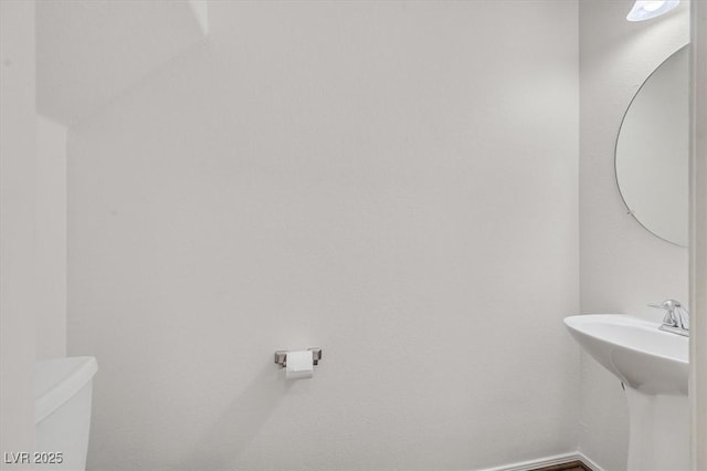 bathroom featuring baseboards, toilet, and a sink