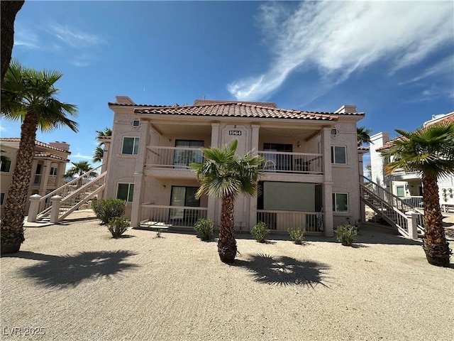 back of property featuring a tiled roof, a balcony, stairs, and stucco siding