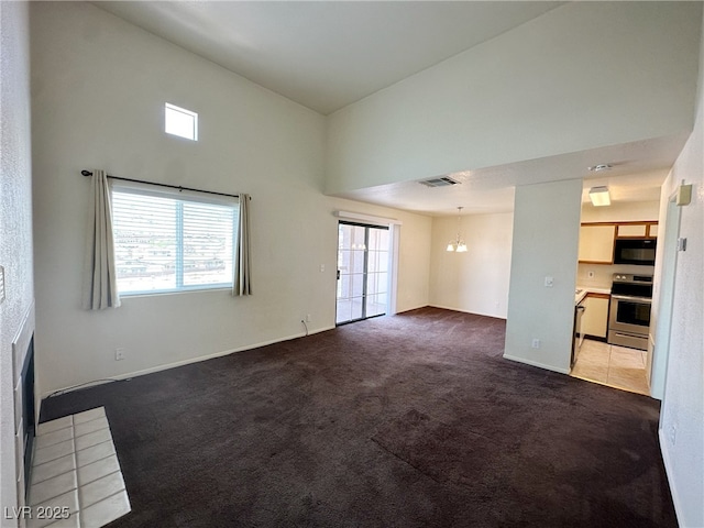 unfurnished living room featuring carpet, a towering ceiling, an inviting chandelier, visible vents, and baseboards