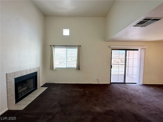 unfurnished living room with carpet flooring, a tiled fireplace, baseboards, a towering ceiling, and visible vents