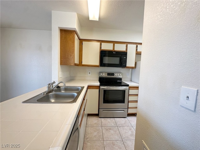 kitchen with a sink, electric range, black microwave, a textured wall, and tile counters