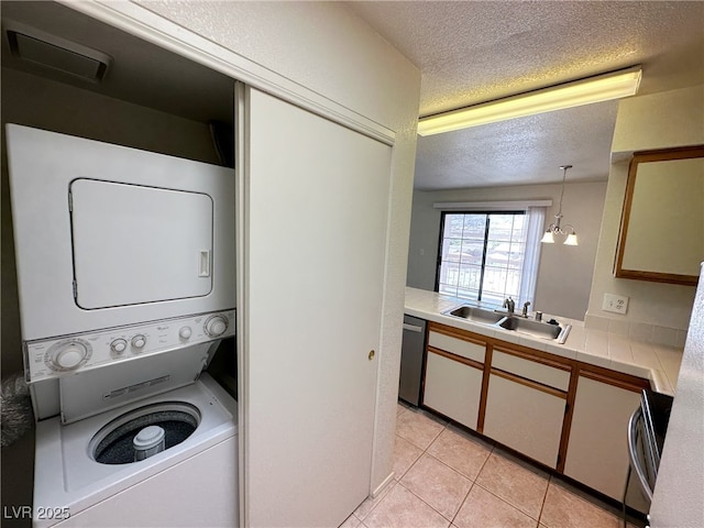 washroom with a sink, a textured ceiling, light tile patterned flooring, stacked washing maching and dryer, and laundry area