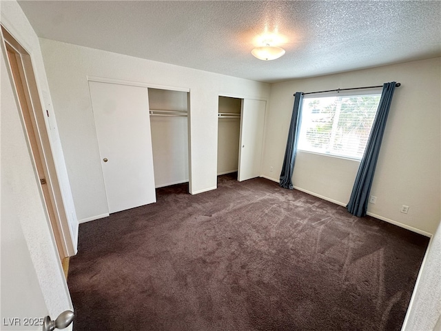 unfurnished bedroom featuring two closets, baseboards, dark carpet, and a textured ceiling