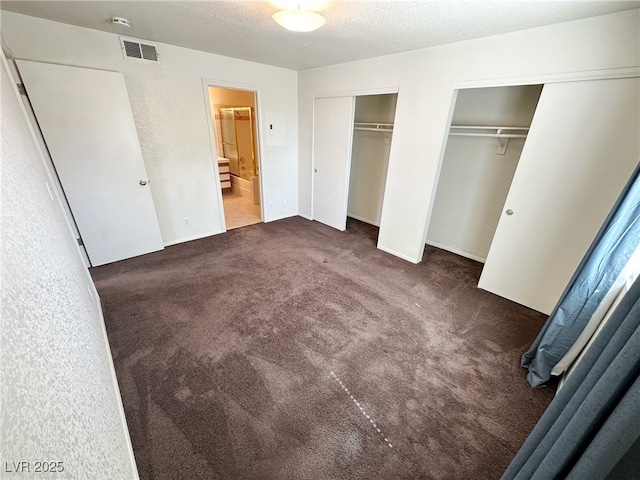unfurnished bedroom with carpet flooring, a textured ceiling, visible vents, two closets, and connected bathroom