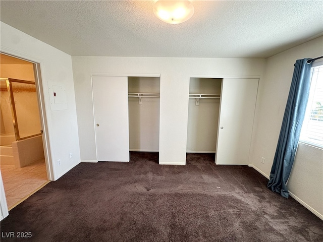 unfurnished bedroom featuring baseboards, carpet flooring, a textured ceiling, and two closets